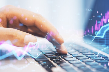 hands using laptop computer keyboard with abstract glowing candlestick forex chart with index and grid on blurry background. Invest, trade, finance ans stock market concept. Double exposure.