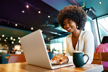 Smiling young african woman sitting with laptop in cafe