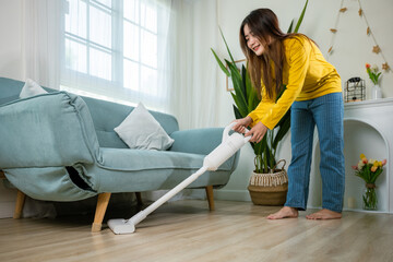 Housewife female dust cleaning floor under sofa or couch furniture with vacuum cleaner, Happy Asian...