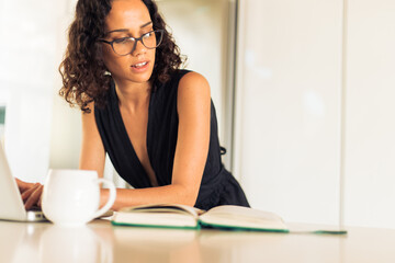 Obraz premium Focused freelancer looking in diary and using laptop in kitchen