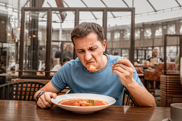 dissatisfied unhappy customer of the restaurant sniffs the disgusting smell of a bowl of soup with spoiled ingredients and is going to complain to the chef - obrazy, fototapety, plakaty