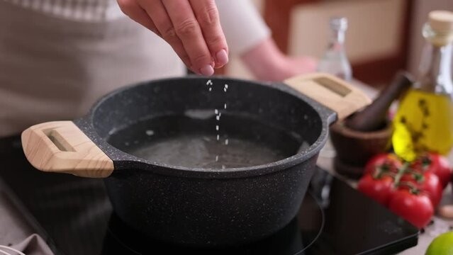 woman adding salt to boiling water in a pot on induction hob at domestic kitchen