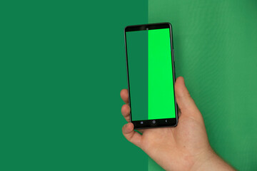 A man's hand on a green background holds a mobile phone with a green screen, a template with a phone, a green screen, a photo before and after cutting the background, an example of a template