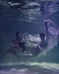 Fototapeta na wymiar fashionable man and woman in glasses underwater on a dark blue background in the pool