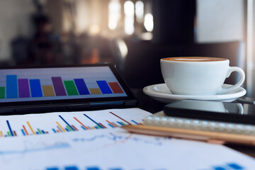 Close up view, latte coffee in white cup with tablet computer with chart on screen and paperwork of investment on table in cafe, Business concept people take a break during a day in cafe and working