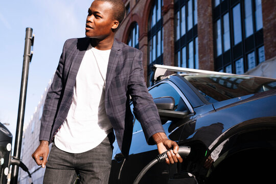 Young man inserting charging plug into electric car