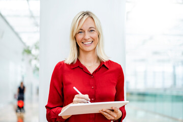 Smiling businesswoman with tablet PC and digitized pen standing in front of column