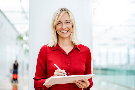 Smiling businesswoman with tablet PC and digitized pen standing in front of column