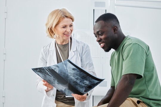 Smiling doctor holding X-ray looking at patient in clinic - Powered by Adobe