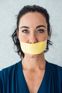 Woman with tape over mouth standing in front of gray wall
