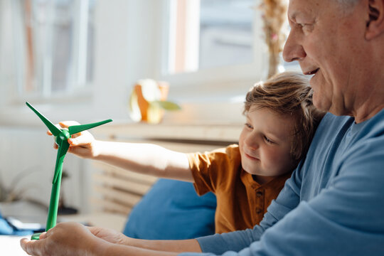 Senior man examining wind turbine model with grandson at home
