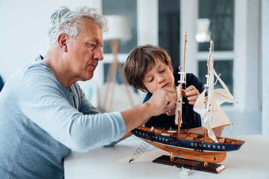 Grandfather and grandson with ship model on table at home