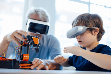 Senior man and boy with VR glasses watching robot model at home