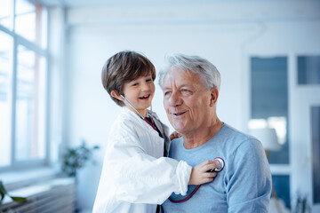 Happy boy imitating as doctor checking grandfather with stethoscope at home