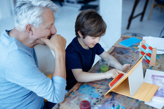 Smiling boy using tablet PC by grandfather at home