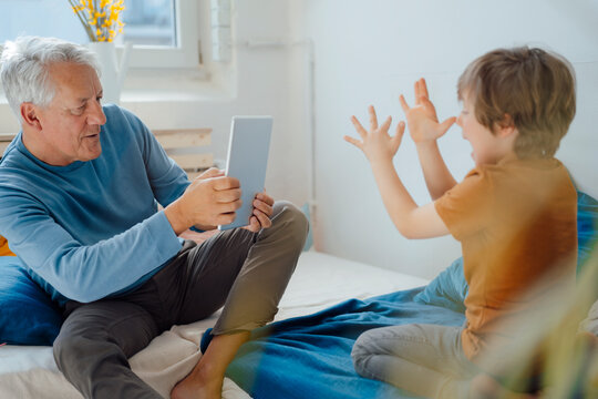 Senior man photographing playful grandson through tablet PC at home
