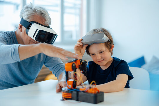 Boy examining robot model by grandfather with VR glasses at home