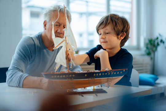 Boy and senior man looking at ship model on table