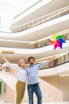 Happy businesswoman with colleague holding pinwheel toy in office lobby