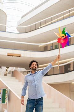 Smiling businessman with hand raised holding pinwheel toy