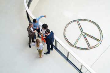 Multiracial business colleagues planning strategies by peace symbol in office corridor