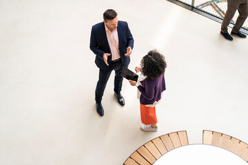 Businessman discussing with colleague holding tablet PC in corridor