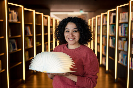 Smiling woman with open book lamp in illuminated library