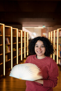 Happy woman with open book lamp in illuminated library