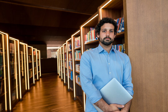 Man with laptop by bookshelf in library