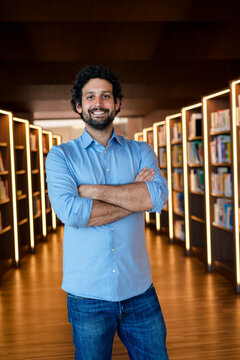 Happy man with arms crossed in illuminated library