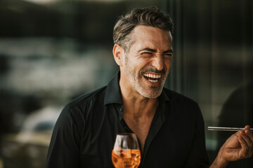 Mature man laughing holding glass of drink