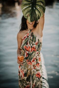 Smiling woman with drink holding monstera leaf
