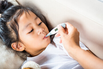 Sick kid. Mother checking temperature of her sick daughter with thermometer in mouth, child laying...