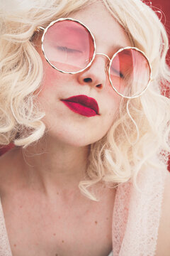 Blond woman with eyes closed wearing red sunglasses
