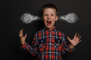 Aggressive little boy with steam coming out of his ears on black background