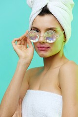  Vertical photo, a woman on a blue background in a towel on her head and body and glasses and patches on her lips