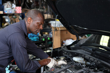 Man technician car mechanic in uniform checking maintenance a car service at repair garage station. Worker holding wrench and fixing breakdown vehicle. Concept of car center repair service.