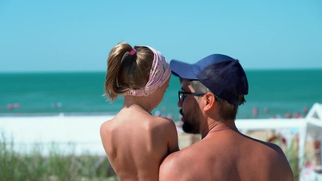 Back view of father and child look at hotel beach with blue sea. Concept of summer vacation, travel, holiday. People outdoors on seascape