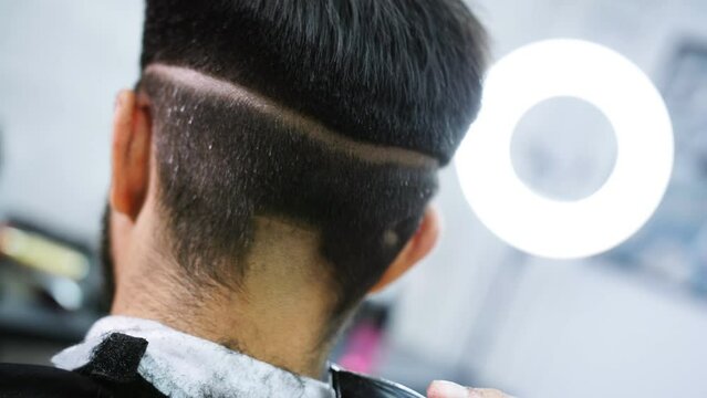 Close up of head of young man getting haircut by hairdresser at stylish barbershop. Image of male hands using professional trimmer and getting perfect shape for vintage haircut of handsome hipster.