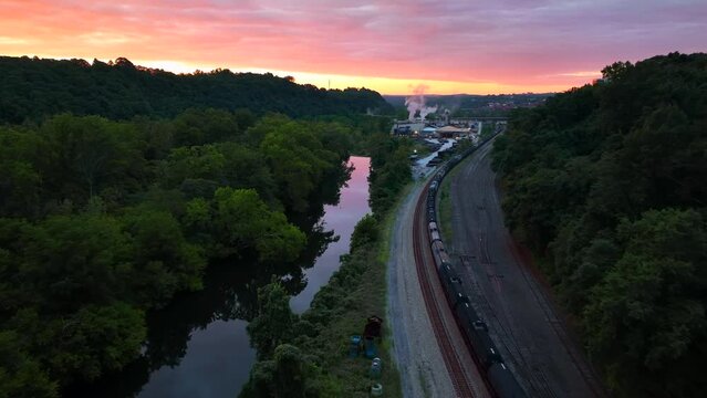 Tanker train cars on railroad track beside river during morning sunrise. Aerial view.