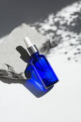 Blue dropper bottles with serum, tonic or essential oil on grey concrete podium. White background with daylight with flowers shadows. Beauty concept for face and body care