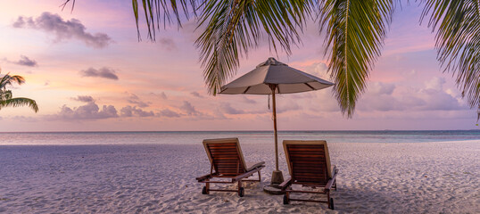 Beautiful tropical island sunset, couple sun beds chairs umbrella under palm tree leaves. White...