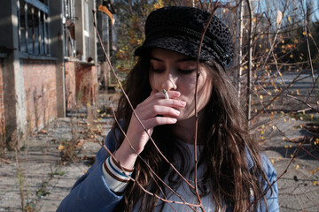 Young brunet smoking a cigarette in front of an abandoned building in autumn