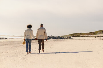 Rearview of an elderly couple walking barefoot on beach sand