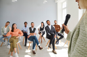 Fototapeta premium Close up of woman speaker or coach hold microphone lead seminar or training for diverse employees. Businesswoman talk speak at group presentation for businesspeople. Business education.