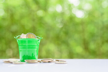 Building wealth and wealth accumulation, financial concept : Coins in a green bucket on a table, depicting the accumulation of wealth overtime that requires money to be made, saved and invested.