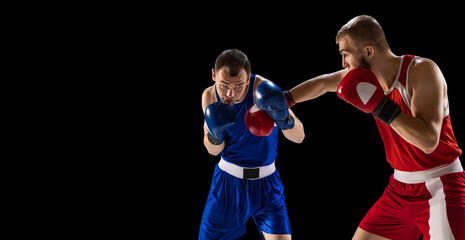 Young men, professional boxers in red and blue sports uniform boxing isolated on dark background. Concept of sport, skills, power, training, energy