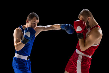Plakat Young men, professional boxers in red and blue sports uniform boxing isolated on dark background. Concept of sport, skills, power, training, energy