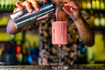man hand bartender making pink cocktail in glass on the bar counter