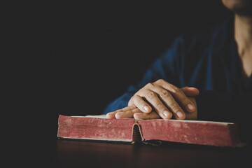 Hand folded in prayer to god on Holy Bible book in church concept for faith, spirituality and...